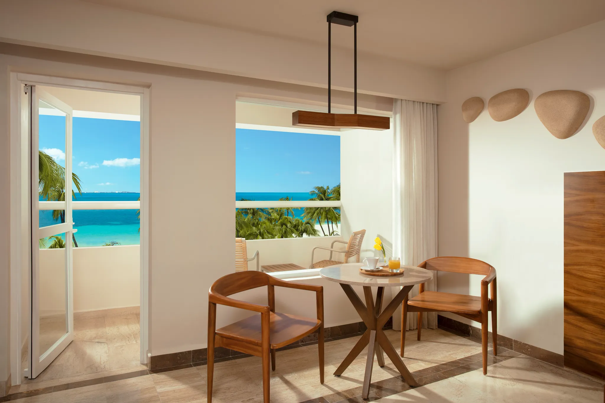Deluxe Partial Ocean View suite dining area with balcony overlooking the Caribbean Sea at Dreams Sands Cancun Resort & Spa.