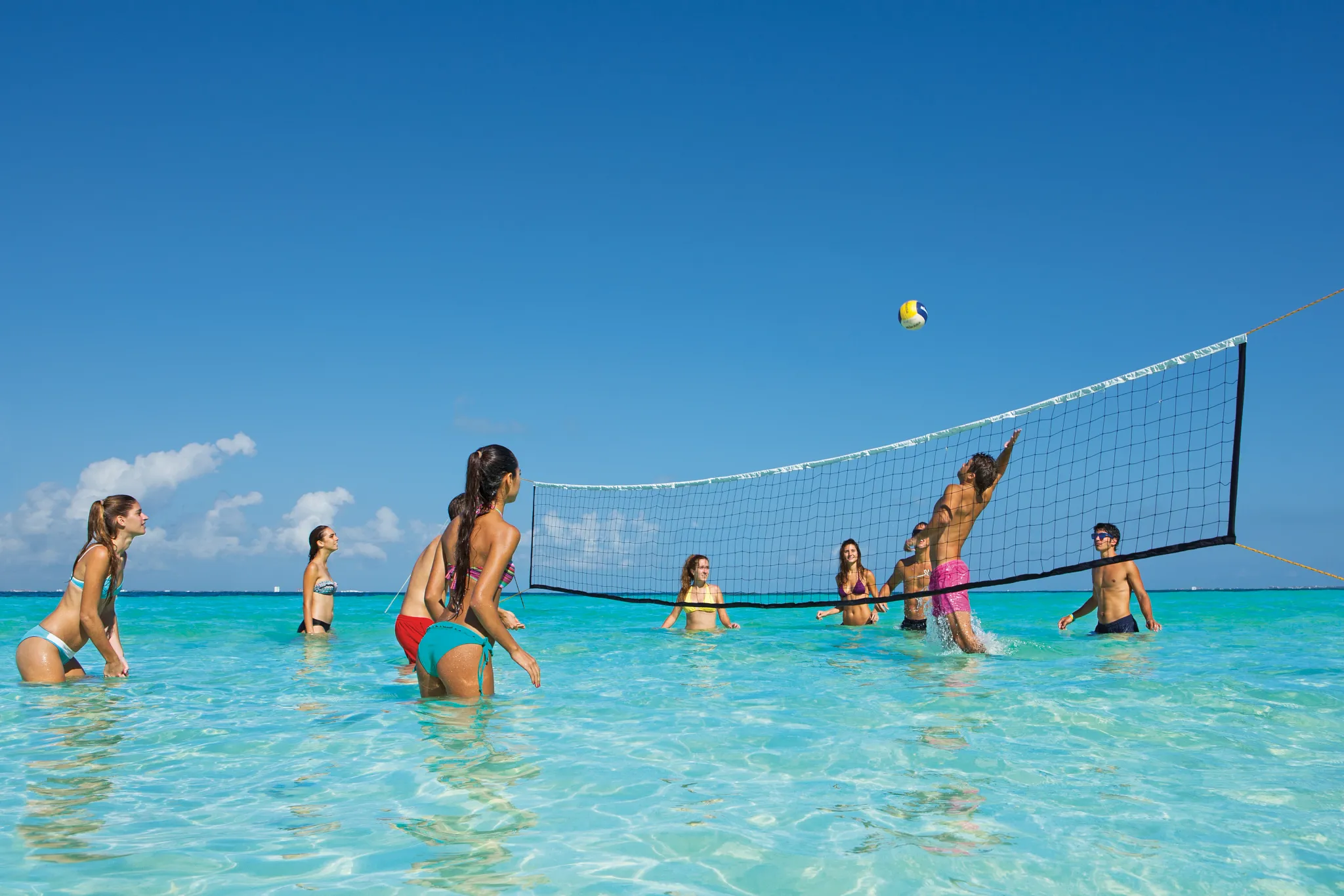 Guests playing beach volleyball in shallow turquoise waters at Dreams Sands Cancun Resort & Spa.