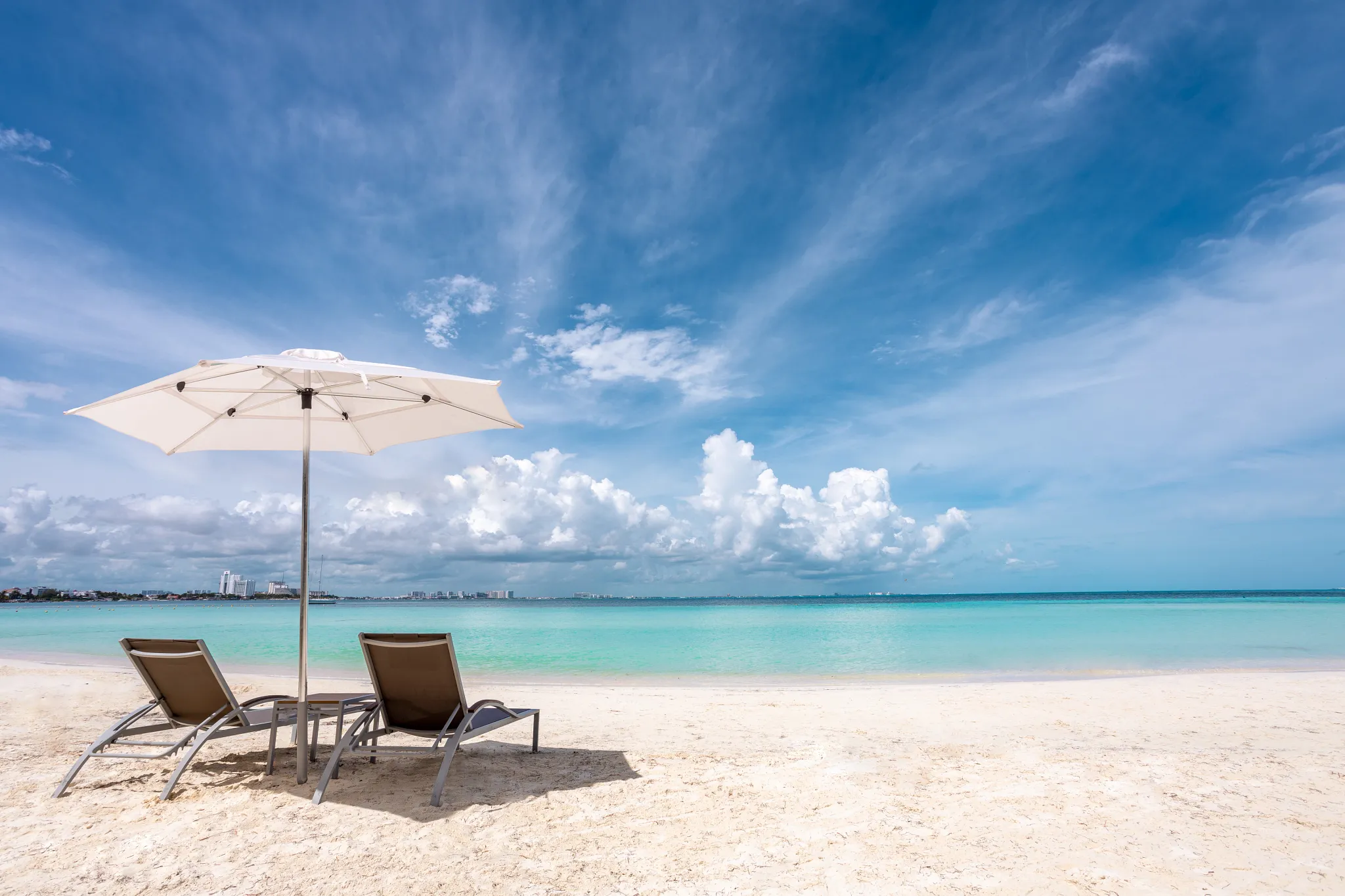 Beach loungers and umbrella overlooking calm turquoise waters at Dreams Sands Cancun Resort & Spa.