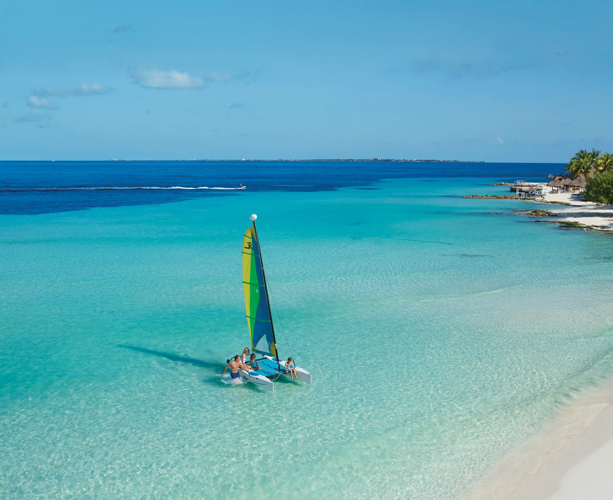 Family enjoying a catamaran sailboat in clear turquoise waters near Dreams Sands Cancun Resort & Spa.